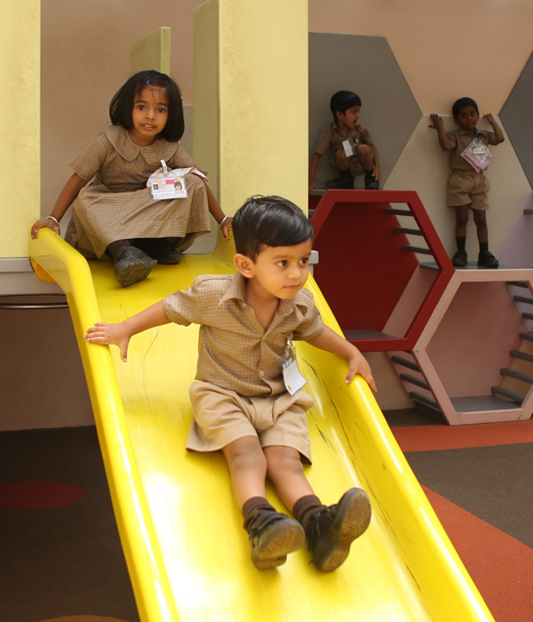 Pre-primary students playing on a yellow slide at Innisfree House School Bangalore
